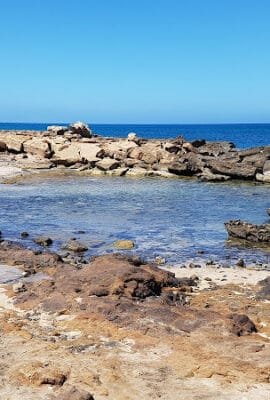 View of Beach Baia Murdeira with Monte Leão rising in the background, calm Atlantic waters, and rocky shoreline under a clear Cape Verde sky.