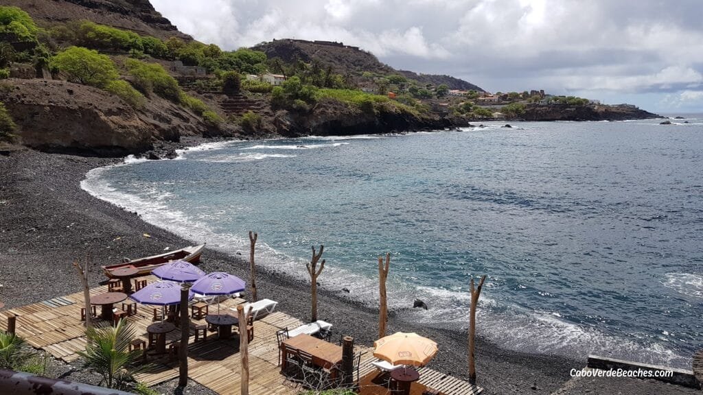 Black sands of Cidade Velha Beach, Cape Verde, meeting the turquoise sea near historic landmarks.