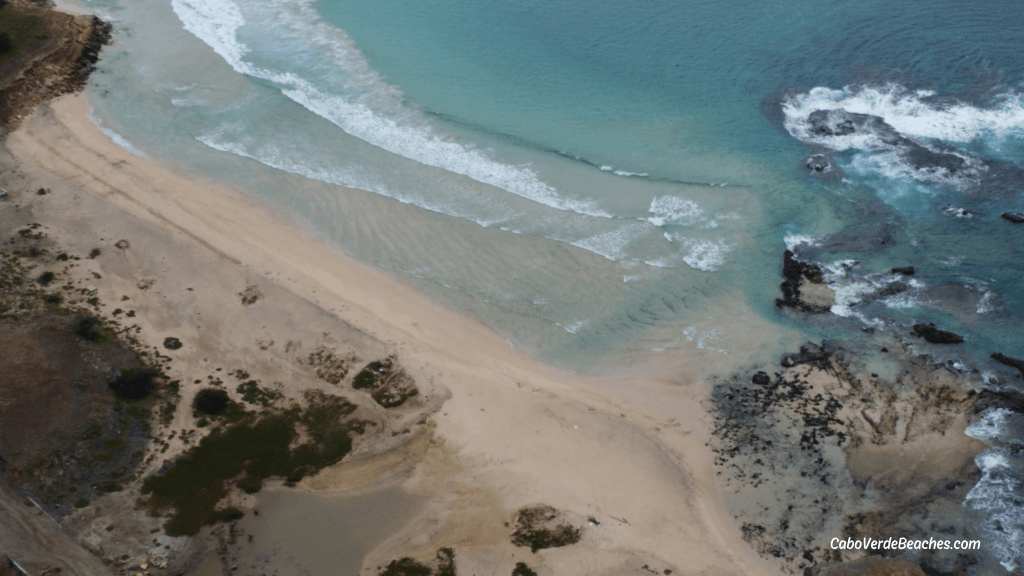 White sandy shore of Ponta Preta Beach with crystal waters and rocky reefs, near Porto Inglês.
