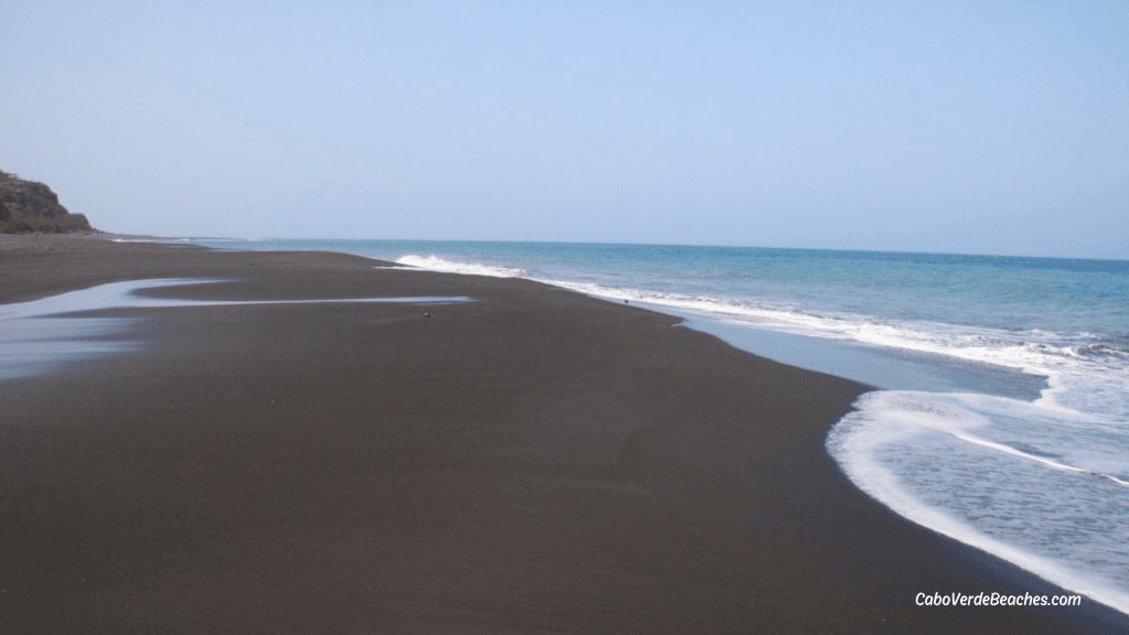 Fonte Bila Beach with black volcanic sand, strong ocean waves, and the view of Brava Island in the background near Praia de Bocarrom, Cape Verde.