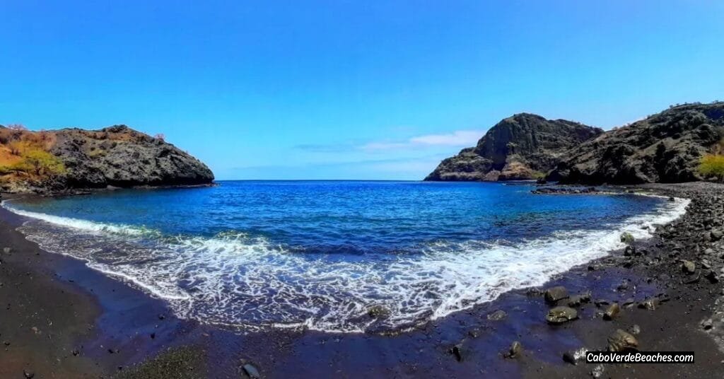 Scenic view of Beach Baia Angra on Santiago Island, Cape Verde, with dark volcanic sand, gentle waves, and lush cliffs surrounding the beach.