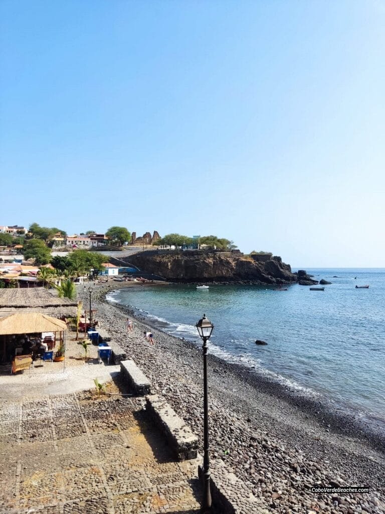 Black sands of Cidade Velha Beach, Cape Verde, meeting the turquoise sea near historic landmarks.