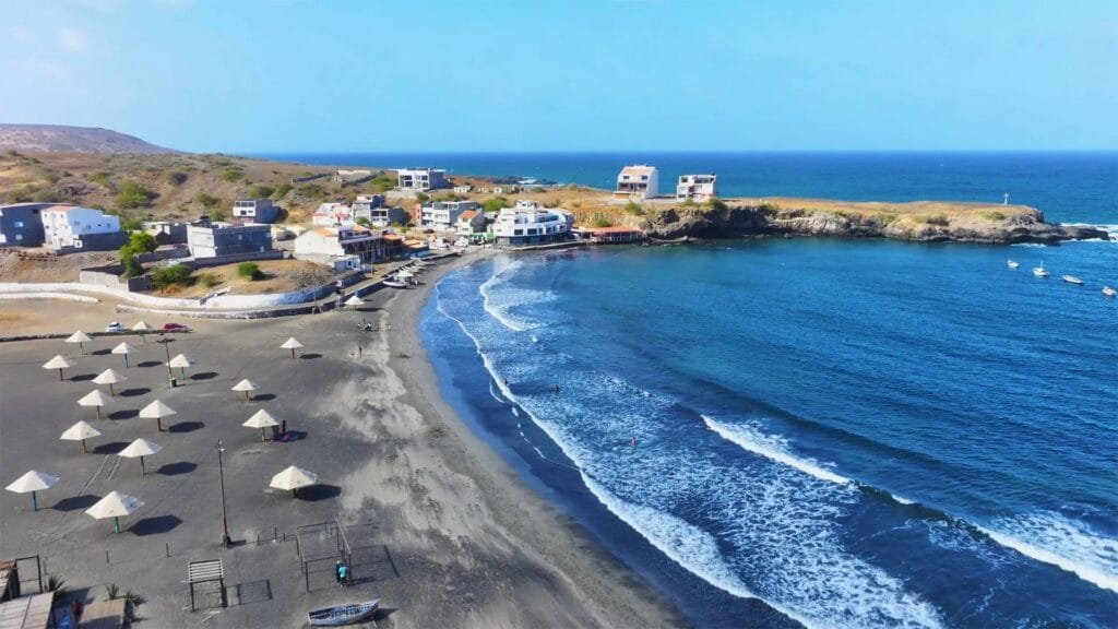 Tranquil Baixo Beach, Cape Verde: Dark sands meet crystal-clear waters under a vibrant sky.