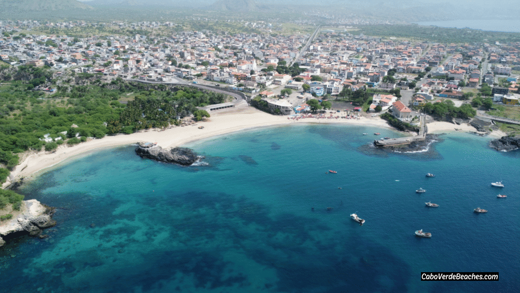 View of Tarrafal Beach in Cape Verde with white sand, turquoise water, and palm trees surrounded by mountains.